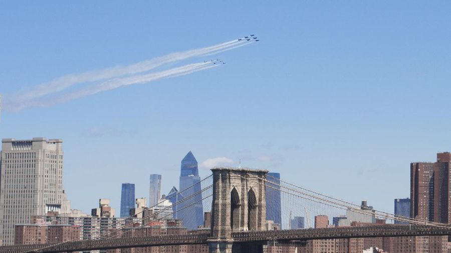 Workers stand on a dirt pile in Red Hook, N.Y., to view the Blue Angels and Thunderbirds flight teams flyover New York City skyline, Tuesday April 28, 2020, in New York. The flyover was in salute to first responders in the fight against the COVID-19 pandemic. (AP Photo/Bebeto Matthews)