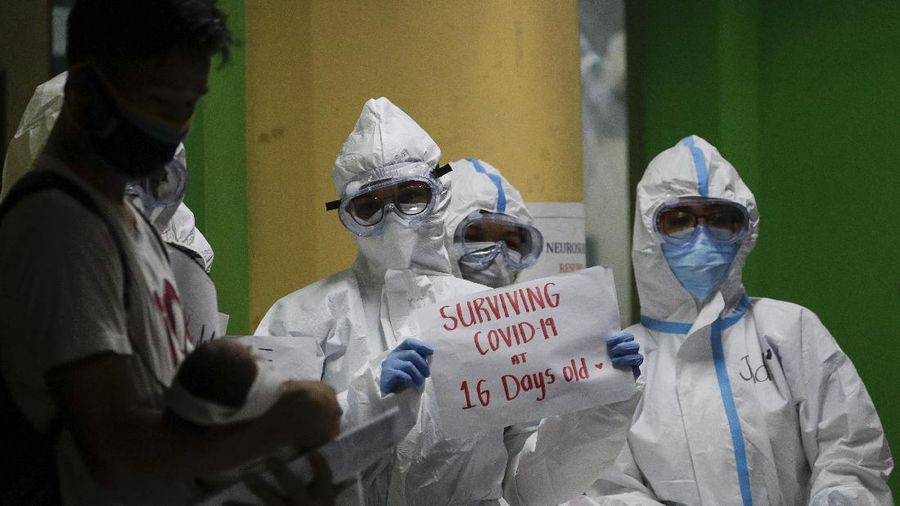Health workers wearing protective suits holds signs beside a 16-day-old baby who recovered from COVID-19 as he is discharged from the National Children's Hospital in Quezon city, Metro Manila, Philippines during a continuing enhanced community quarantine to prevent the spread of the new coronavirus on Tuesday, April 28, 2020. The baby nicknamed 