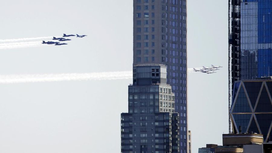 Workers stand on a dirt pile in Red Hook, N.Y., to view the Blue Angels and Thunderbirds flight teams flyover New York City skyline, Tuesday April 28, 2020, in New York. The flyover was in salute to first responders in the fight against the COVID-19 pandemic. (AP Photo/Bebeto Matthews)