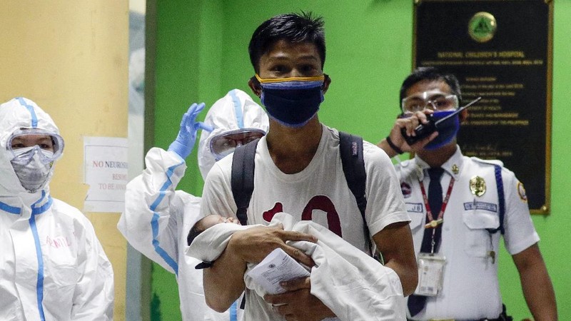 Health workers wearing protective suits holds signs beside a 16-day-old baby who recovered from COVID-19 as he is discharged from the National Children's Hospital in Quezon city, Metro Manila, Philippines during a continuing enhanced community quarantine to prevent the spread of the new coronavirus on Tuesday, April 28, 2020. The baby nicknamed 