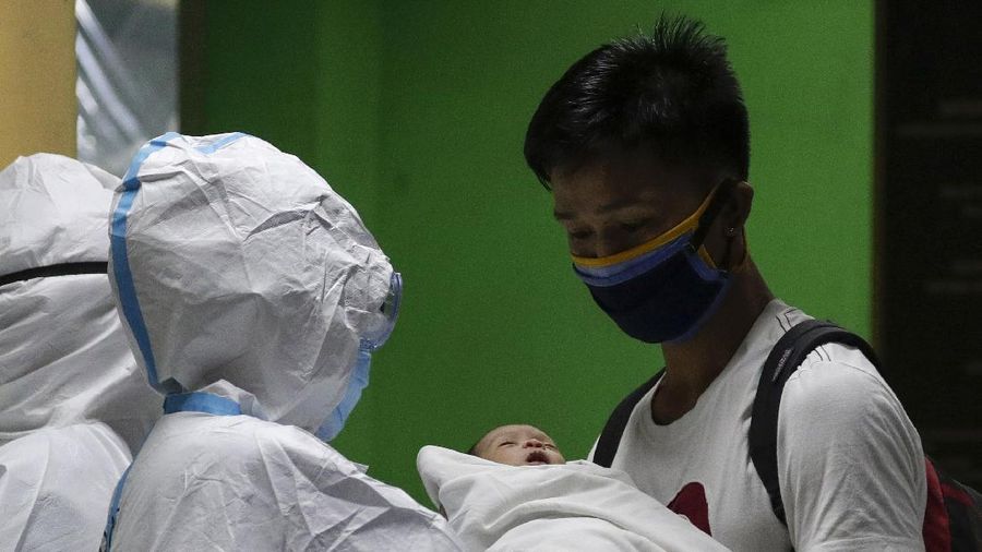 Health workers wearing protective suits holds signs beside a 16-day-old baby who recovered from COVID-19 as he is discharged from the National Children's Hospital in Quezon city, Metro Manila, Philippines during a continuing enhanced community quarantine to prevent the spread of the new coronavirus on Tuesday, April 28, 2020. The baby nicknamed 