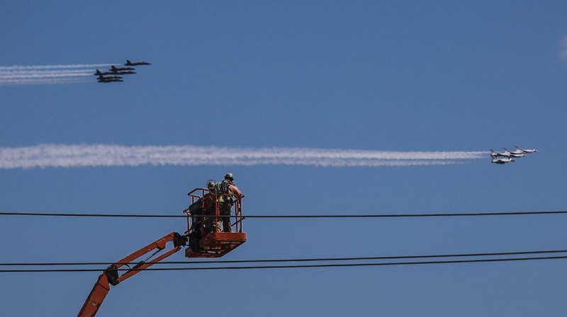 Workers stand on a dirt pile in Red Hook, N.Y., to view the Blue Angels and Thunderbirds flight teams flyover New York City skyline, Tuesday April 28, 2020, in New York. The flyover was in salute to first responders in the fight against the COVID-19 pandemic. (AP Photo/Bebeto Matthews)