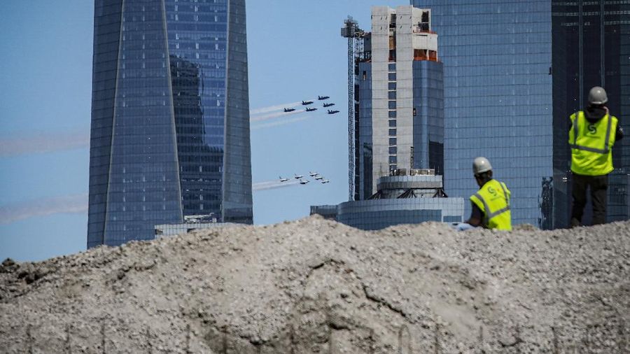 Workers stand on a dirt pile in Red Hook, N.Y., to view the Blue Angels and Thunderbirds flight teams flyover New York City skyline, Tuesday April 28, 2020, in New York. The flyover was in salute to first responders in the fight against the COVID-19 pandemic. (AP Photo/Bebeto Matthews)