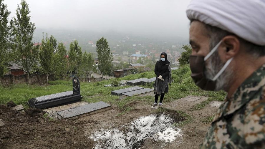 A woman wearing a mask and gloves prays at the grave of her mother who died from the new coronavirus, at a cemetery in the outskirts of the city of Babol, in north of Iran, Thursday, April 30, 2020. (AP Photo/Ebrahim Noroozi)