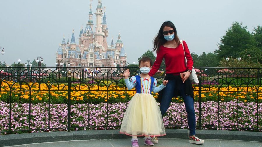 Visitors, wearing face masks, wait to enter the Disneyland theme park in Shanghai as it reopened, Monday, May 11, 2020. Visits will be limited initially and must be booked in advance, and the company said it will increase cleaning and require social distancing in lines for the various attractions. With warmer weather and new coronavirus cases and deaths falling to near-zero, China has been reopening tourist sites such as the Great Wall and the Forbidden City palace complex in Beijing.(AP Photo/Sam McNeil)