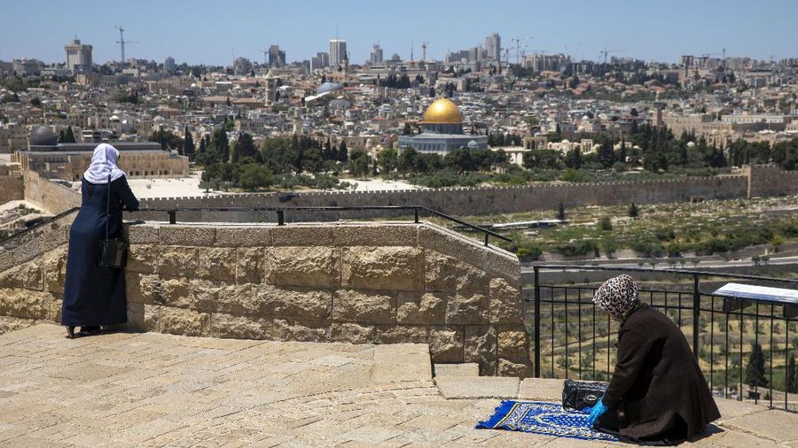 A Muslim woman wears gloves prays in east Jerusalem's Mount of Olives, overlooking the Dome of the Rock and al-Aqsa mosque compound, which remains shut to prevent the spread of coronavirus during the holy month of Ramadan, Friday, May 1, 2020. (AP Photo/Ariel Schalit)