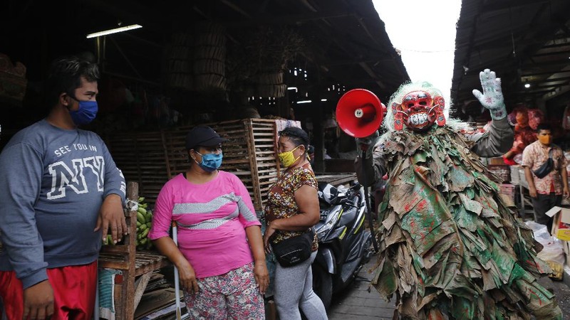A police officer wearing a Balinese traditional mask, called celuluk, performs as the new coronavirus during a campaign to wear masks as a precaution against the virus outbreak at a market in Bali, Indonesia, Thursday, May 14, 2020. (AP Photo/Firdia Lisnawati)