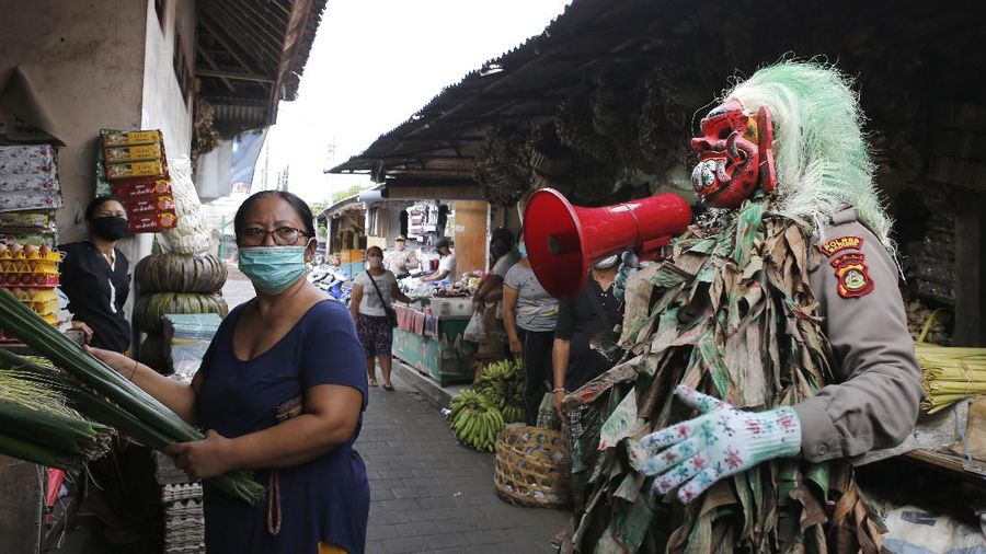 A police officer wearing a Balinese traditional mask, called celuluk, performs as the new coronavirus during a campaign to wear masks as a precaution against the virus outbreak at a market in Bali, Indonesia, Thursday, May 14, 2020. (AP Photo/Firdia Lisnawati)