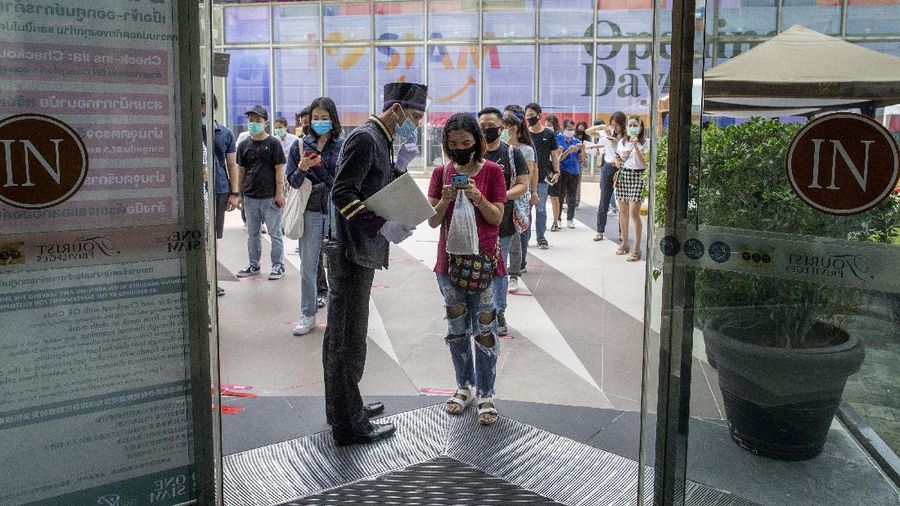 A woman displays her phone to doorman, to conform using a mobile application to help contact-tracing at the entrance to the upmarket shopping mall Siam Paragon in Bangkok, Thailand, Sunday, May 17, 2020. Thai authorities allowed department stores, shopping malls and other businesses to reopen from Sunday, selectively easing restrictions meant to combat the coronavirus. (AP Photo/ Gemunu Amarasinghe)