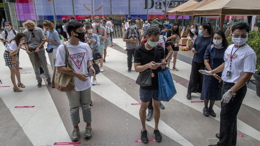 Patrons stand maintaining a physical distance at the entrance of the upmarket shopping mall Siam Paragon in Bangkok, Thailand, Sunday, May 17, 2020. Thai authorities allowed department stores, shopping malls and other businesses to reopen from Sunday, selectively easing restrictions meant to combat the coronavirus. (AP Photo/ Gemunu Amarasinghe)