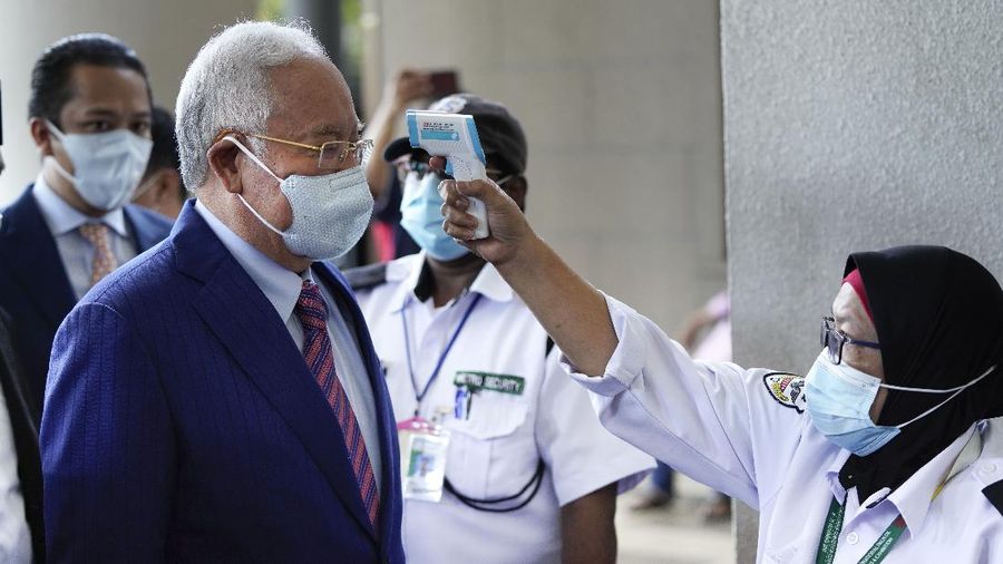 Former Malaysian Prime Minister Najib Razak, left, wearing a face mask has his body temperature checked by a security as he arrives at Kuala Lumpur high court in Kuala Lumpur, Malaysia, Tuesday, May 19, 2020. His trial linked to the multibillion-dollar looting of the 1MDB state investment fund resumed Tuesday. (AP Photo/Vincent Thian)