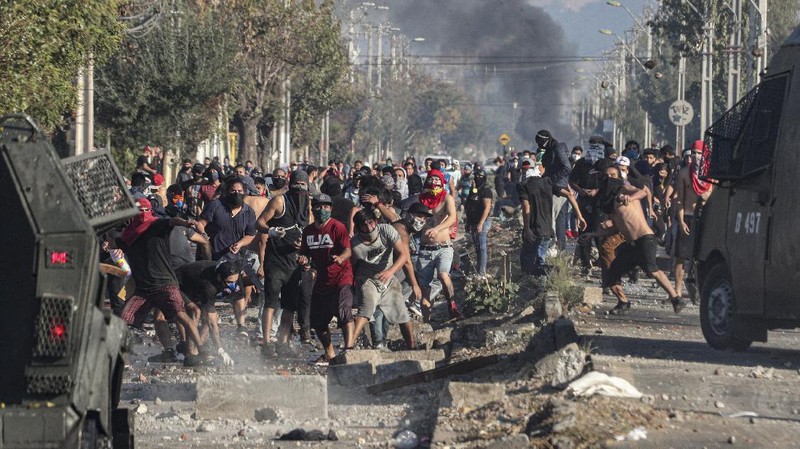Demonstrators, some wearing protective face masks amid the new coronavirus pandemic, clash with the police during a protest demanding food aid from the government, at a poor neighborhood in Santiago, Chile, Monday, May 18, 2020. (AP Photo/Esteban Felix)