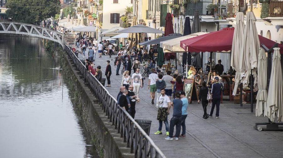 People walk at the Naviglio grande canal district in Milan, Italy, Monday, May 18, 2020. On Monday, Italians enjoyed a first day of regained freedoms, including being able to sit down at a cafe or restaurant, shop in all retail stores or attend church services such as Mass. (AP Photo/Luca Bruno)