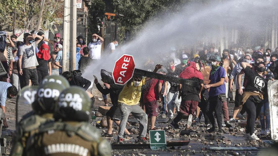 Demonstrators, some wearing protective face masks amid the new coronavirus pandemic, clash with the police during a protest demanding food aid from the government, at a poor neighborhood in Santiago, Chile, Monday, May 18, 2020. (AP Photo/Esteban Felix)