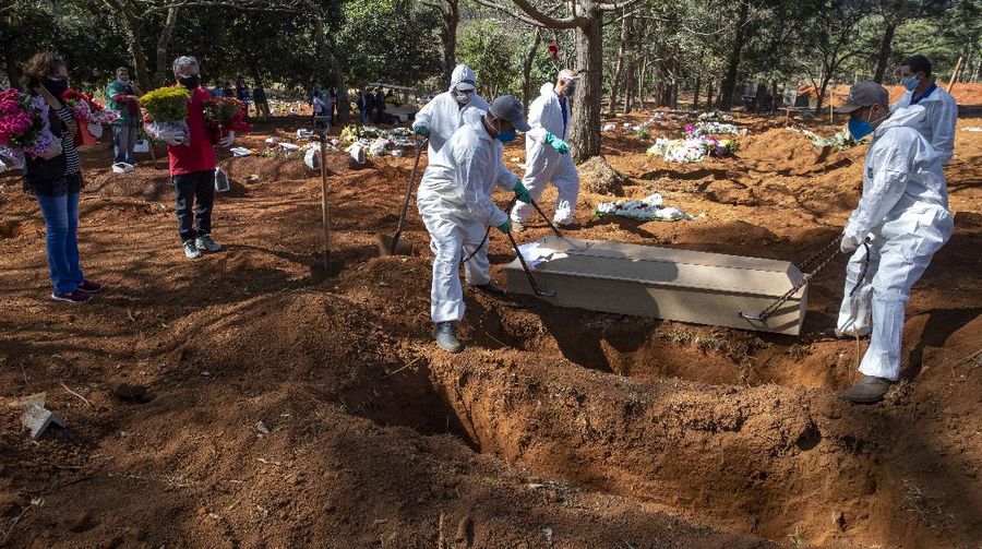 Cemetery workers in protective clothing lower the coffin of 82-year-old Antonio Grossa, who died of COVID-19, as people stand by with flowers at the Vila Formosa cemetery in Sao Paulo, Brazil, Wednesday, May 20, 2020. (AP Photo/Andre Penner)