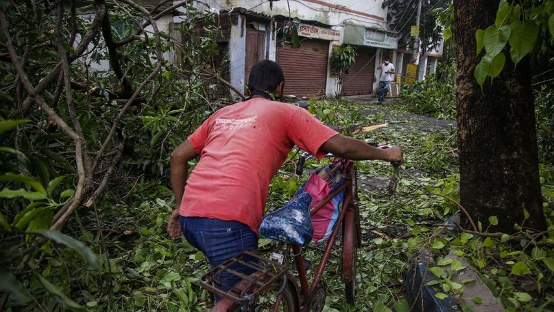 A man makes his way tpast a tree fallen in the middle of a road after Cyclone Amphan hit the region in Kolkata, India, Thursday, May 21, 2020. A powerful cyclone ripped through densely populated coastal India and Bangladesh, blowing off roofs and whipping up waves that swallowed embankments and bridges and left entire villages without access to fresh water, electricity and communications. (AP Photo/Bikas Das)