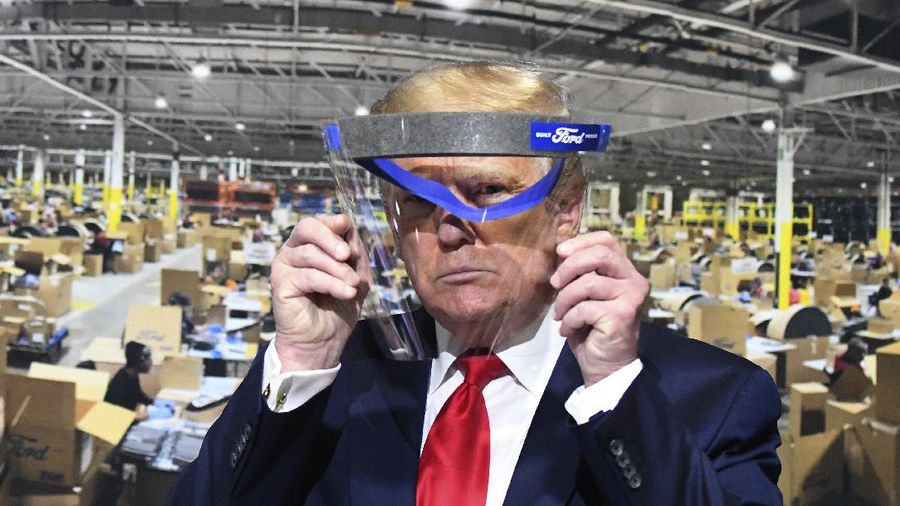 President Donald Trump looks through a face shield, in front of a poster of the manufacturing of the shields, while touring Ford Motor Co.'s Rawsonville Components Plant in Ypsilanti, Michigan on Thursday, May 21, 2020. (Daniel Mears/Detroit News via AP)