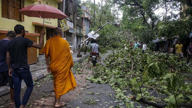 A man makes his way tpast a tree fallen in the middle of a road after Cyclone Amphan hit the region in Kolkata, India, Thursday, May 21, 2020. A powerful cyclone ripped through densely populated coastal India and Bangladesh, blowing off roofs and whipping up waves that swallowed embankments and bridges and left entire villages without access to fresh water, electricity and communications. (AP Photo/Bikas Das)