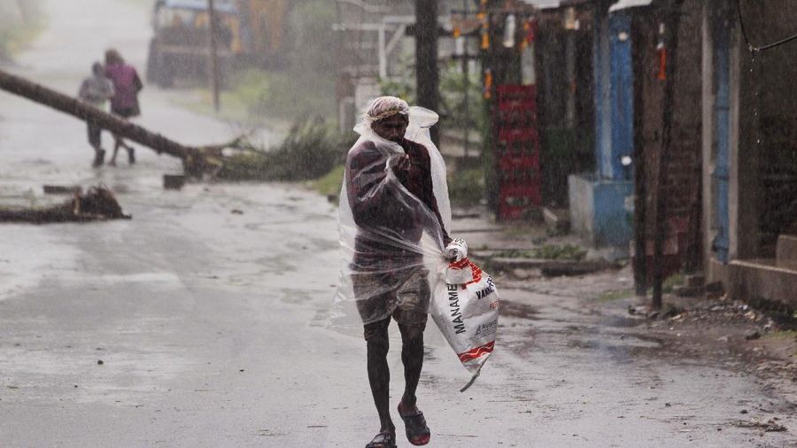 A man makes his way tpast a tree fallen in the middle of a road after Cyclone Amphan hit the region in Kolkata, India, Thursday, May 21, 2020. A powerful cyclone ripped through densely populated coastal India and Bangladesh, blowing off roofs and whipping up waves that swallowed embankments and bridges and left entire villages without access to fresh water, electricity and communications. (AP Photo/Bikas Das)