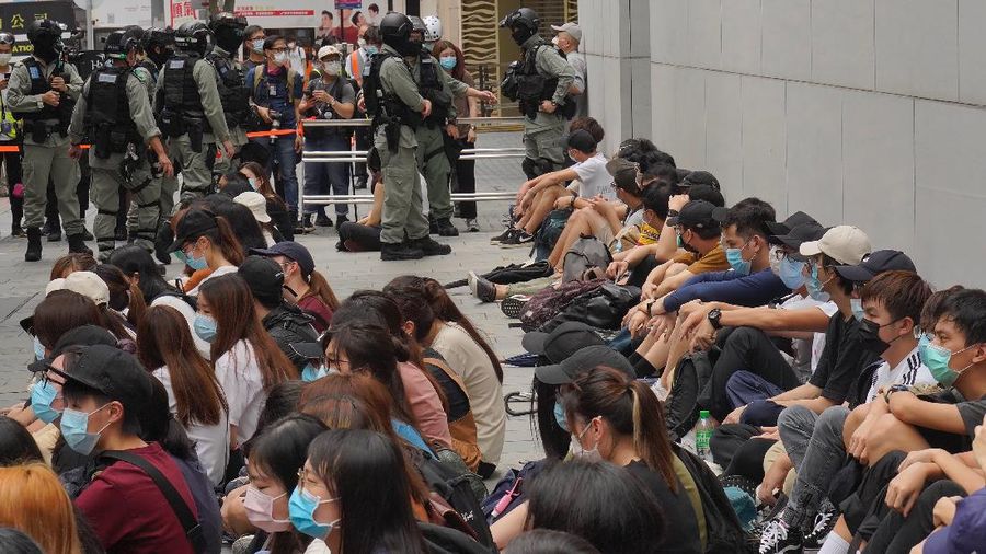 Riot police standing guard as a woman tries to cross the street in the Central district of Hong Kong, Wednesday, May 27, 2020. Hong Kong police massed outside the legislature complex Wednesday, ahead of debate on a bill that would criminalize abuse of the Chinese national anthem in the semi-autonomous city. (AP Photo/Vincent Yu)