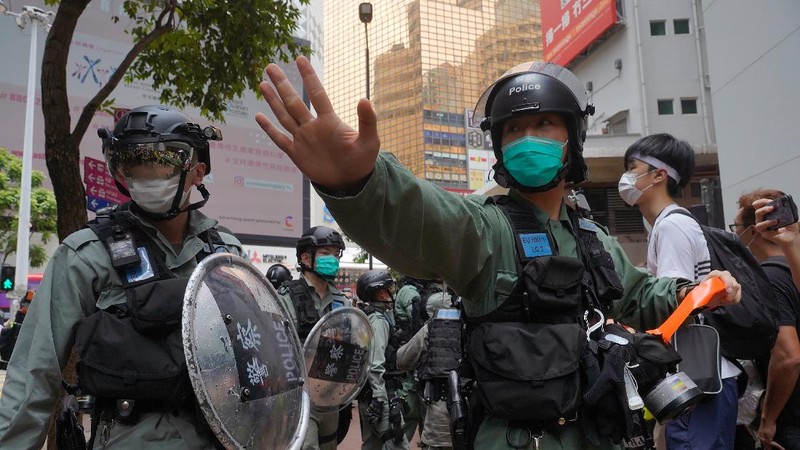 Riot police standing guard as a woman tries to cross the street in the Central district of Hong Kong, Wednesday, May 27, 2020. Hong Kong police massed outside the legislature complex Wednesday, ahead of debate on a bill that would criminalize abuse of the Chinese national anthem in the semi-autonomous city. (AP Photo/Vincent Yu)