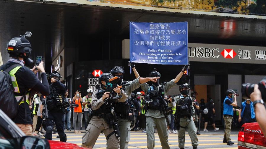 Riot police standing guard as a woman tries to cross the street in the Central district of Hong Kong, Wednesday, May 27, 2020. Hong Kong police massed outside the legislature complex Wednesday, ahead of debate on a bill that would criminalize abuse of the Chinese national anthem in the semi-autonomous city. (AP Photo/Vincent Yu)