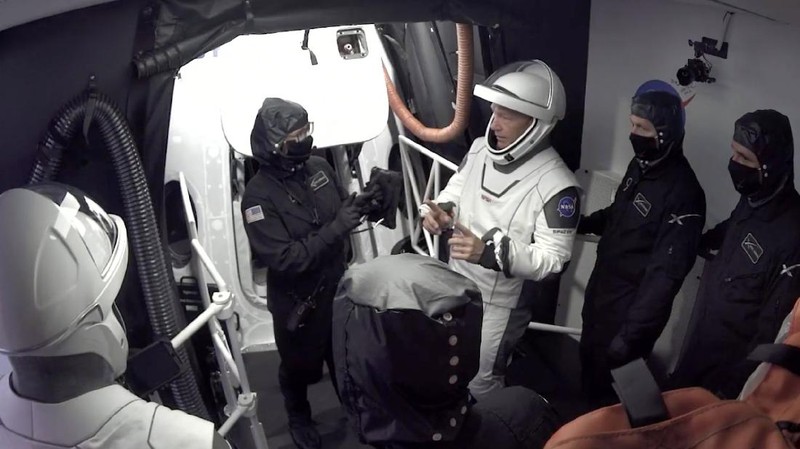 In this Wednesday, May 27, 2020 image from video made available by SpaceX, NASA astronauts  Doug Hurley, center, and Bob Behnken, left, confer with technicians after leaving the Crew Dragon capsule at the Kennedy Space Center in Cape Canaveral, Fla., after an aborted launch due to weather problems. (SpaceX via AP)