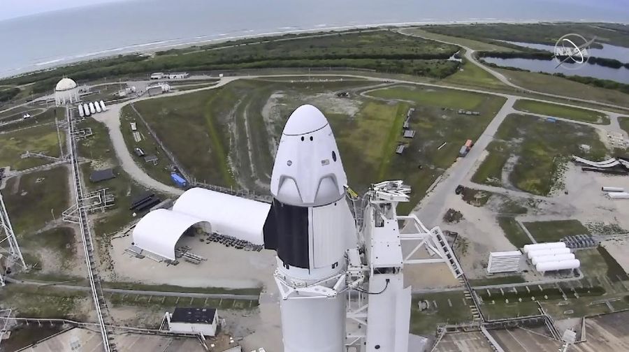 In this Wednesday, May 27, 2020 image from video made available by SpaceX, NASA astronauts  Doug Hurley, center, and Bob Behnken, left, confer with technicians after leaving the Crew Dragon capsule at the Kennedy Space Center in Cape Canaveral, Fla., after an aborted launch due to weather problems. (SpaceX via AP)