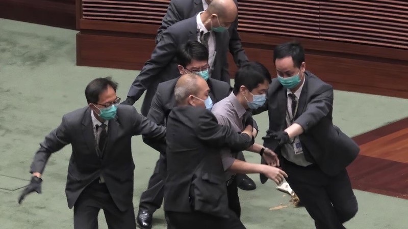 Staff from the Legislative Council cover the floor with towels after a pro-democracy lawmaker hurled an object during the second day of debate on a bill that would criminalize insulting or abusing the Chinese anthem in Hong Kong, Thursday, May 28, 2020. The lawmaker ejected later had spilled a substance on the floor that had to be cleaned up by firefighters wearing protective gear.(AP Photo/Vincent Yu)