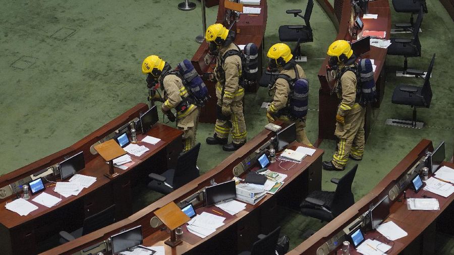 Staff from the Legislative Council cover the floor with towels after a pro-democracy lawmaker hurled an object during the second day of debate on a bill that would criminalize insulting or abusing the Chinese anthem in Hong Kong, Thursday, May 28, 2020. The lawmaker ejected later had spilled a substance on the floor that had to be cleaned up by firefighters wearing protective gear.(AP Photo/Vincent Yu)