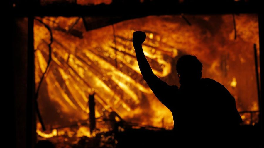 A protester gestures in front of the burning 3rd Precinct building of the Minneapolis Police Department on Thursday, May 28, 2020, in Minneapolis. Protests over the death of George Floyd, a black man who died in police custody Monday, broke out in Minneapolis for a third straight night. (AP Photo/Julio Cortez)