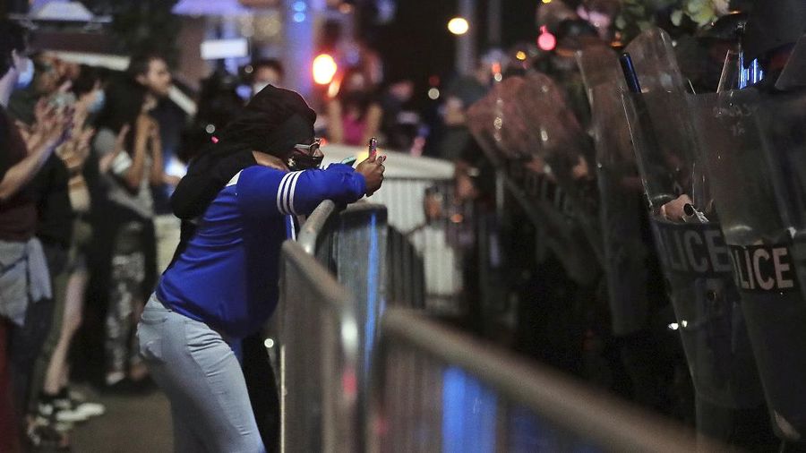 A protester gestures in front of the burning 3rd Precinct building of the Minneapolis Police Department on Thursday, May 28, 2020, in Minneapolis. Protests over the death of George Floyd, a black man who died in police custody Monday, broke out in Minneapolis for a third straight night. (AP Photo/Julio Cortez)