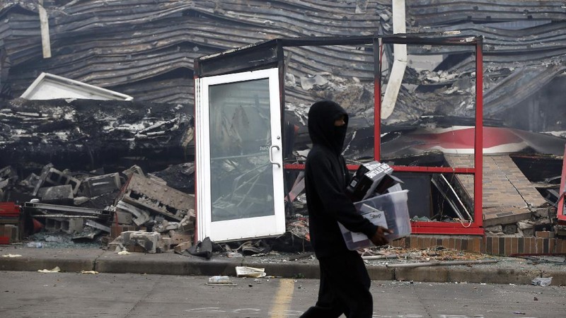A protester gestures in front of the burning 3rd Precinct building of the Minneapolis Police Department on Thursday, May 28, 2020, in Minneapolis. Protests over the death of George Floyd, a black man who died in police custody Monday, broke out in Minneapolis for a third straight night. (AP Photo/Julio Cortez)
