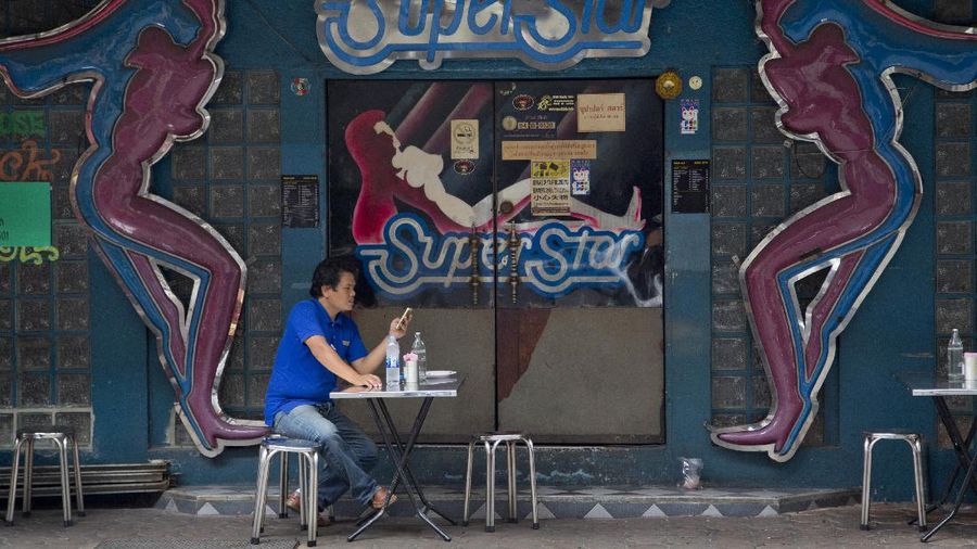 A man sitting outside an adult entertainment establishment in the Patpong nightlife area looks at his mobile phone after eating a meal in Bangkok, Thailand, Thursday, July 5, 2018. (AP Photo/Gemunu Amarasinghe)