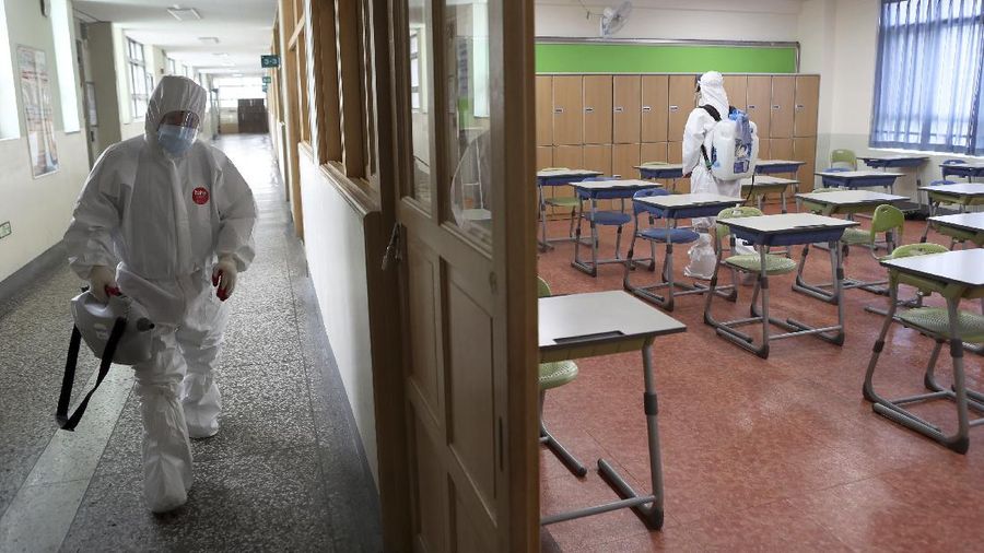 Workers wearing protective gear disinfect as a precaution against the new coronavirus in a class at a high school in Busan, South Korea, Saturday, May 30, 2020. (Jo Jung-ho/Yonhap via AP)