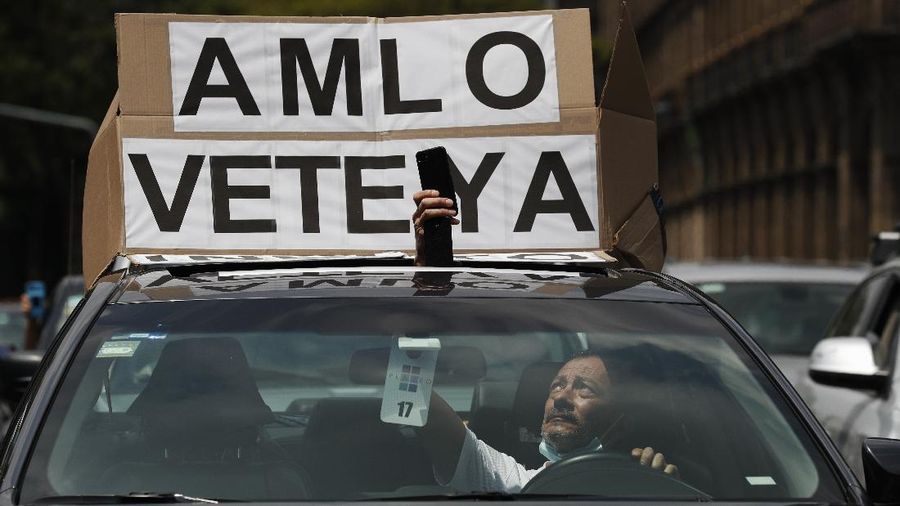 A man drives a car with a sign reading in Spanish; 