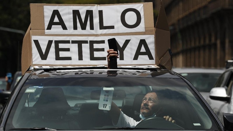 A man drives a car with a sign reading in Spanish; 
