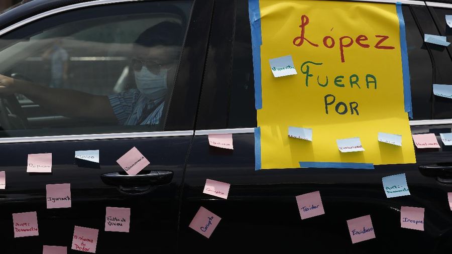 A man drives a car with a sign reading in Spanish; 