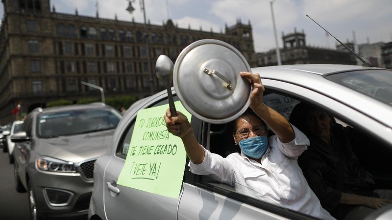 A man drives a car with a sign reading in Spanish; 
