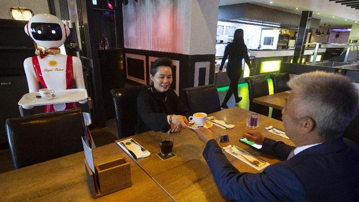 Owners Shu Lei Hu, left, and her husband Shao Song Hu, right, demonstrate the use of robots for serving purposes or for dirty dishes collection, as part of a tryout of measures to respect social distancing and help curb the spread of the COVID-19 coronavirus, at the family's Royal Palace restaurant in Renesse, south-western Netherlands, Wednesday, May 27, 2020. (AP Photo/Peter Dejong)