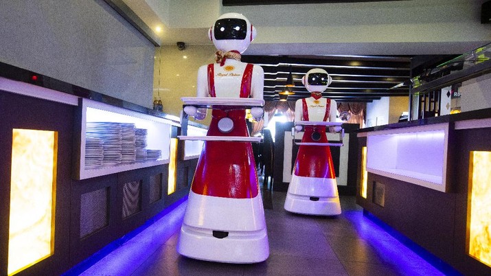 Restoran dengan Pelayanan Robot (AP/Peter Dejong) Owners Shu Lei Hu, left, and her husband Shao Song Hu, right, demonstrate the use of robots for serving purposes or for dirty dishes collection, as part of a tryout of measures to respect social distancing and help curb the spread of the COVID-19 coronavirus, at the family's Royal Palace restaurant in Renesse, south-western Netherlands, Wednesday, May 27, 2020. (AP Photo/Peter Dejong)