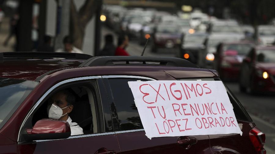 A man drives a car with a sign reading in Spanish; 