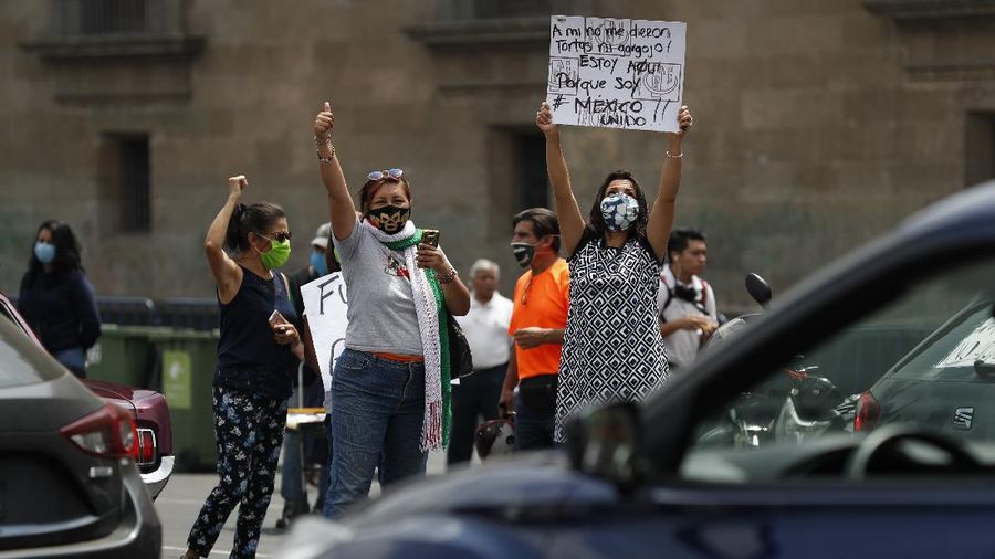 A man drives a car with a sign reading in Spanish; 