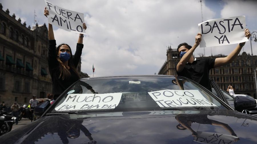 A man drives a car with a sign reading in Spanish; 