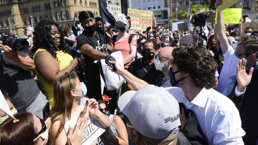 Prime Minister Justin Trudeau shakes hands with a participant who gave him a Black Lives Matter T-shirt as he takes part in an anti-racism protest on Parliament Hill during the coronavirus pandemic in Ottawa, Ontario, Friday, June 5, 2020. The death of George Floyd, a black man who died after he was restrained by Minneapolis police officers on May 25, has ignited protests in the U.S. and worldwide over racial injustice and police brutality. (Sean Kilpatrick/The Canadian Press via AP)