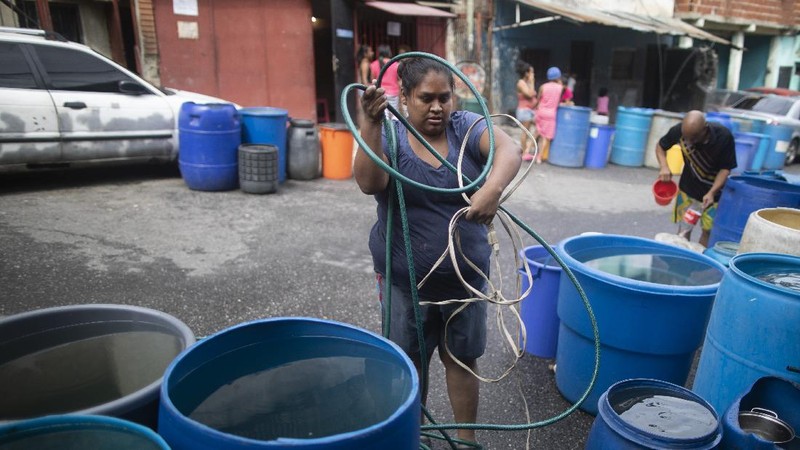 A woman untangles an electrical cord and a hose in order to pump from a large container water provided by a government water truck, in the Petare slum of Caracas, Venezuela, Wednesday, June 10, 2020. Amid water shortages during the COVID-19 pandemic, the government is providing free water to some areas. (AP Photo/Ariana Cubillos)