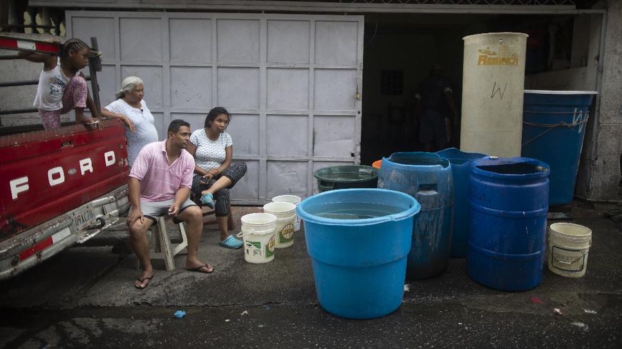 A woman untangles an electrical cord and a hose in order to pump from a large container water provided by a government water truck, in the Petare slum of Caracas, Venezuela, Wednesday, June 10, 2020. Amid water shortages during the COVID-19 pandemic, the government is providing free water to some areas. (AP Photo/Ariana Cubillos)