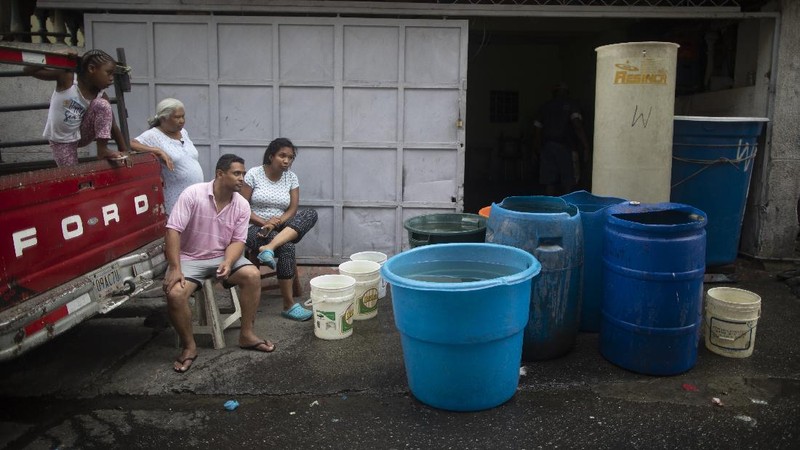 A woman untangles an electrical cord and a hose in order to pump from a large container water provided by a government water truck, in the Petare slum of Caracas, Venezuela, Wednesday, June 10, 2020. Amid water shortages during the COVID-19 pandemic, the government is providing free water to some areas. (AP Photo/Ariana Cubillos)