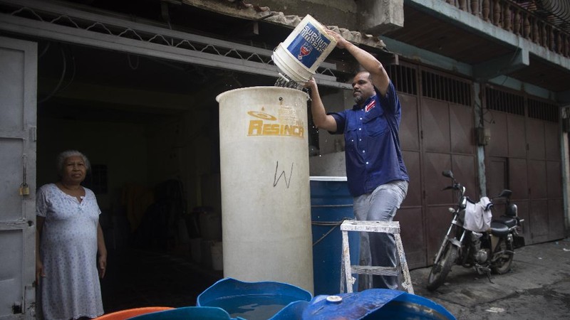 A woman untangles an electrical cord and a hose in order to pump from a large container water provided by a government water truck, in the Petare slum of Caracas, Venezuela, Wednesday, June 10, 2020. Amid water shortages during the COVID-19 pandemic, the government is providing free water to some areas. (AP Photo/Ariana Cubillos)