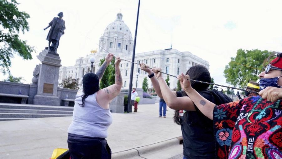Activists bring down the Christopher Columbus statue in front of the Capitol, Wednesday, June 10, 2020, in St. Paul, Minn. A rope was thrown around the 10-foot bronze statue and it was pulled off its stone pedestal. The protesters included Dakota and Ojibwe Indians who consider Columbus as a symbol of genocide against Native Americans. State Patrol troopers in helmets stood by at a distance but did not try to stop the protesters. (Leila Navidi/Star Tribune via AP)
